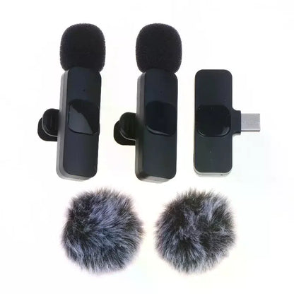 Two black wireless lapel microphones with foam windshields, shown alongside a USB-C receiver and two gray furry microphone windshields on a white background.