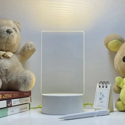 Desk setup with a lamp, teddy bear, books, and small notebook on a white surface. LED acrylic message board with light-up writing