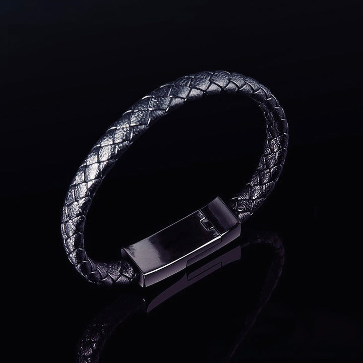 A dark metallic braided Wearable smartphone charging cable bracelet with a polished rectangular clasp, displayed on a reflective black surface.